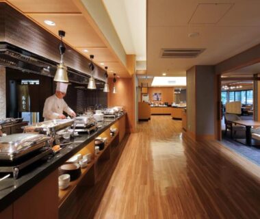 Chefs preparing dishes behind buffet counter with wood flooring and lounge seating in Kamogawakan, Chiba