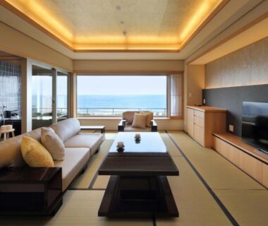 Tatami room with low table, sofa and large windows overlooking the sea at Kamogawakan, Chiba