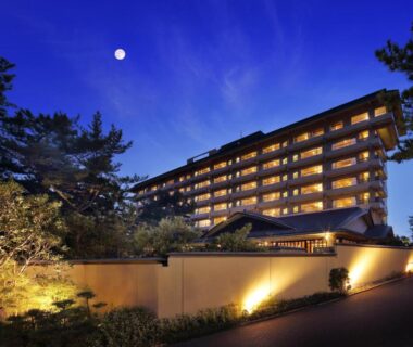 Dusk view of lit multi-story ryokan building, landscaped entrance and moonlit sky in Chiba, Kantō