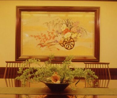 Ikebana centerpiece on a glossy lacquer table with framed Japanese wall painting and wooden chairs at Kamogawakan, Kyoto