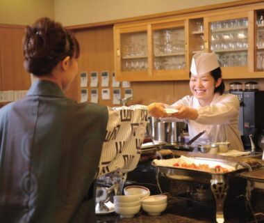 Staff serving a hot beverage behind a wooden counter with glassware at Kamogawakan in Chiba