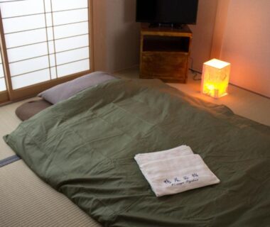 Futon laid on tatami mat beside shoji screens with soft lamp and folded towel at Kamoya Ryokan, Kyoto