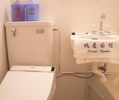 Compact bathroom with toilet, sink and towel labeled Kamoya Ryokan in Kyoto