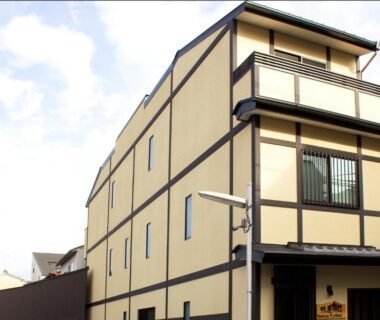 Beige three-story ryokan facade with dark wooden trim and small entrance on a Kyoto street