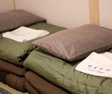 Stacked futon mattresses and pillows with folded linens on tatami at Kamoya Ryokan in Kyoto