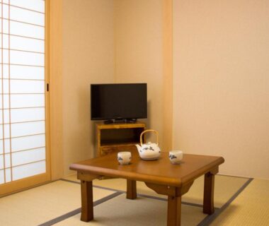 Traditional tatami room with low wooden table, tea set, shoji screen and television at Kamoya Ryokan in Kyoto