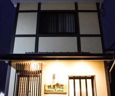 Night exterior of compact multi-story ryokan with illuminated doorway, Kamoya Ryokan, Kyoto, Kansai
