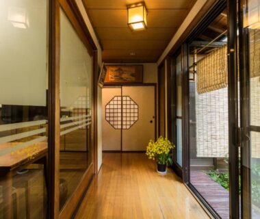 Wooden corridor with shoji-style door, glass panels, bamboo blinds and potted yellow flowers overlooking a small garden