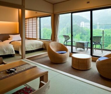 Spacious tatami seating area with low table, twin beds and balcony overlooking green hills at Kanaya Hotel Kinugawa