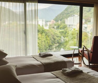 Two beds and chair by window overlooking river valley and town at Kanaya Hotel Kinugawa, Tochigi, Kantō