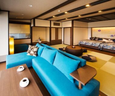 Spacious tatami room with turquoise sofa, low wooden table and bedding on tatami at Kanazawa Hyakurakusou, Ishikawa