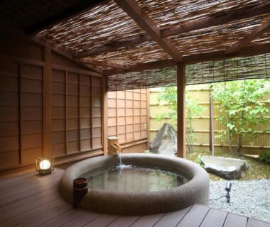 Circular stone bath with wooden deck and bamboo screen at Kanazawa Yuwaku Onsen Kokarian, Ishikawa