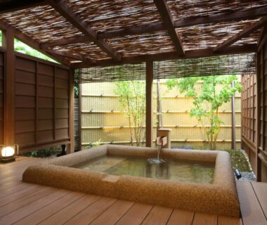 Stone-lined outdoor onsen bath on wooden deck with bamboo screen at Kanazawa Yuwaku Onsen Kokarian, Ishikawa