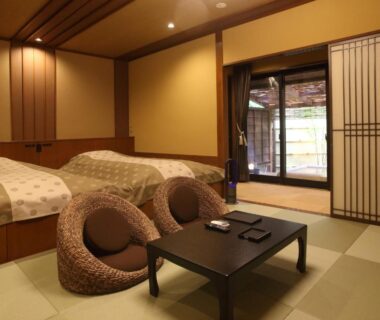 Tatami room with low table, round floor chairs, twin beds and garden doorway at Kanazawa Yuwaku Onsen Kokarian