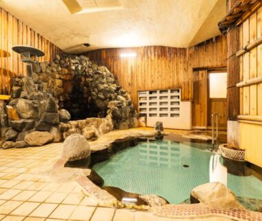 Tiled indoor onsen pool with rock grotto, wooden walls and lockers at Kaneki Hotel in Nagano