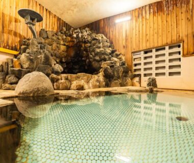 Rock-lined indoor onsen bath with wooden walls and tiled floor at Kaneki Hotel, Nagano