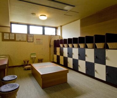 Changing area with black and white lockers, low wooden bench, round stools and washbasins under small windows