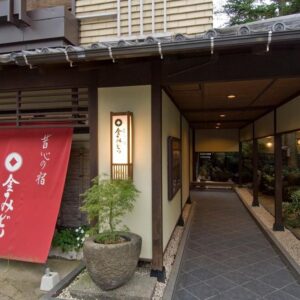 Covered entrance walkway with red noren, stone path and traditional wooden facade at Kanemidori ryokan, Gunma