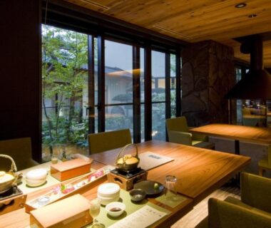 Wood-paneled dining room with tabletop hotpots, suspended hood and garden view at Kanemidori in Gunma