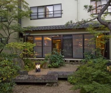 Stone courtyard with lanterns and manicured greenery outside Kanemidori traditional windows in Gunma