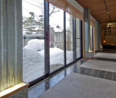 Interior corridor with floor-to-ceiling windows overlooking a snow-covered garden at Kanemidori in Gunma Kantō