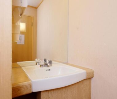 Compact wooden vanity sink with mirror and beige walls at Kanko Hotel Tamaru in Nara
