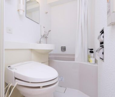 Compact white bathroom with electronic bidet toilet, small sink and bathtub with shower curtain