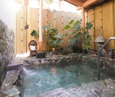 Stone-lined onsen with bamboo fence, plants, handrail and tanuki statue at Kanko Ryokan Kuboji in Nara