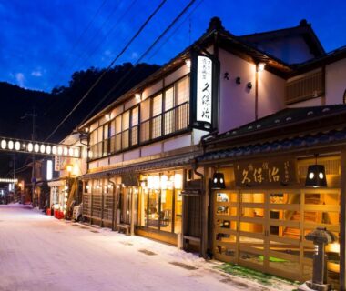 Evening frontage of Kanko Ryokan Kuboji along a snowy street in Nara, lanterns and wooden shopfronts