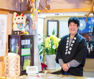 Smiling staff member in traditional attire behind reception desk at Kanko Ryokan Kuboji in Nara