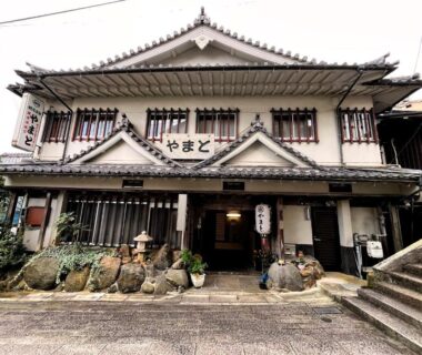 Traditional two-story ryokan facade with wooden lattice windows, stone lanterns and entrance at Kanko Ryokan Yamato, Nara