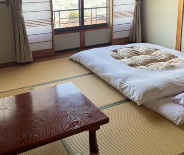 Traditional tatami room with folded futon and low wooden table, shoji screens and window at Kanko Ryokan Yamato Nara