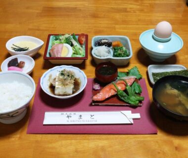 Traditional Japanese breakfast set with salmon, rice, miso soup, tofu, egg, and pickles on red tray
