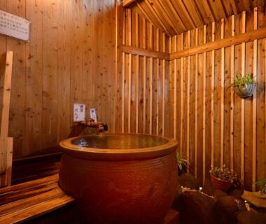 Circular soaking tub in wooden-sided bath alcove with slatted walls and potted plants at Kannawa Yunoka Oita
