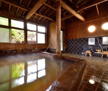 Traditional indoor onsen with wooden beams, stone bath and washing stations at Kannawa Yunoka in Ōita