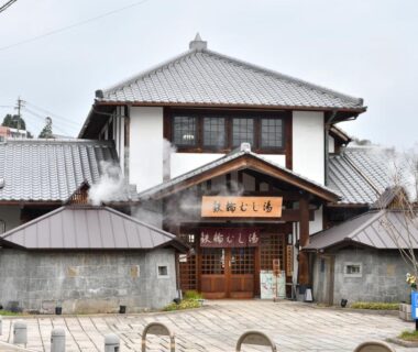 Two-story traditional ryokan with tiled roof, wooden entrance and steam rising from vents at Kannawa Yunoka, Ōita