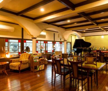 Wooden-floor lounge with piano, sofas and dining tables at Kannawa Yunoka in Ōita, Kyūshū