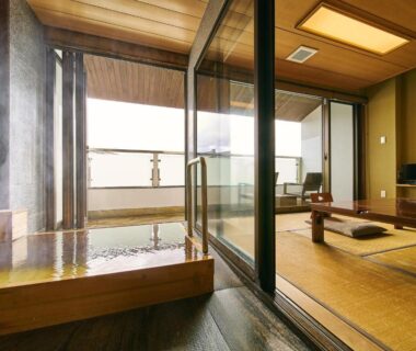 Tatami room with low table and zabuton, adjacent wooden soaking tub opening onto balcony
