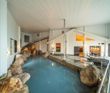 Spacious indoor onsen bath with natural rock features and seating at Kannawaen, Ōita