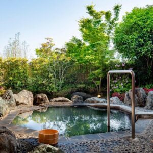 Stone-framed outdoor onsen bath with wooden bucket and handrail at Kannawaen in Ōita, Kyūshū, Japan