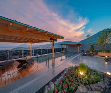 Rooftop open-air onsen terrace with wooden deck, lounge chairs, small stone garden and distant mountain view at dusk