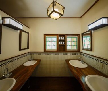 Communal wash area with multiple sinks, wooden counters, mirrors and decorative windows at Kannomori, Ōita