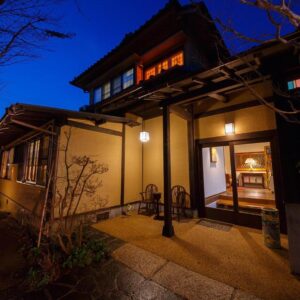 Lit traditional ryokan entrance with wooden beams and shoji doorway at Kannomori Oita Kyushu
