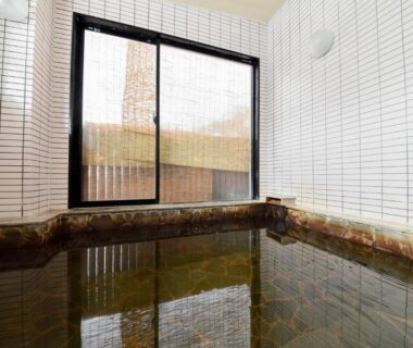 Tiled indoor onsen bath with wooden edging and window at Kanoe ryokan in Nagano