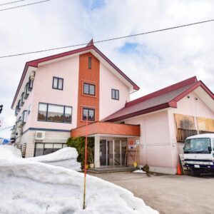 Exterior of Kanoe ryokan with snowbanks and parked guest vans at the entrance in Nagano, Chūbu region