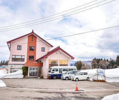 Snow-covered three-story ryokan exterior with parked vans near entrance, Kanoe, Nagano in Chūbu