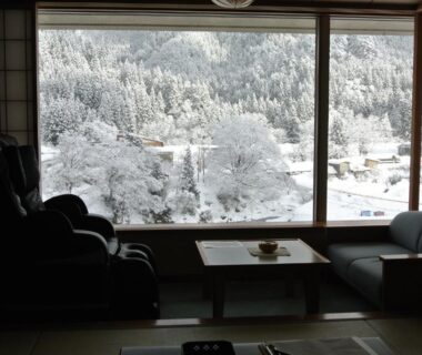 Tatami seating, low table and chairs facing snow-covered forest through large window at Kansyokan Yamagata