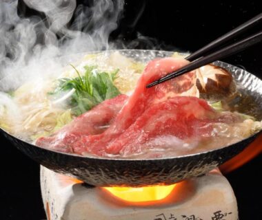Thinly sliced beef simmering in a tabletop hot pot with greens and chopsticks at Kansyokan, Yamagata
