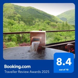 Outdoor onsen bath with wooden spout and glass railing overlooking green mountains at Kansyokan, Yamagata