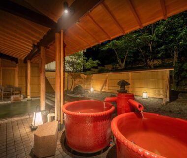 Outdoor red ceramic onsen tubs beneath wooden roof beside garden at Kansyokan, Yamagata